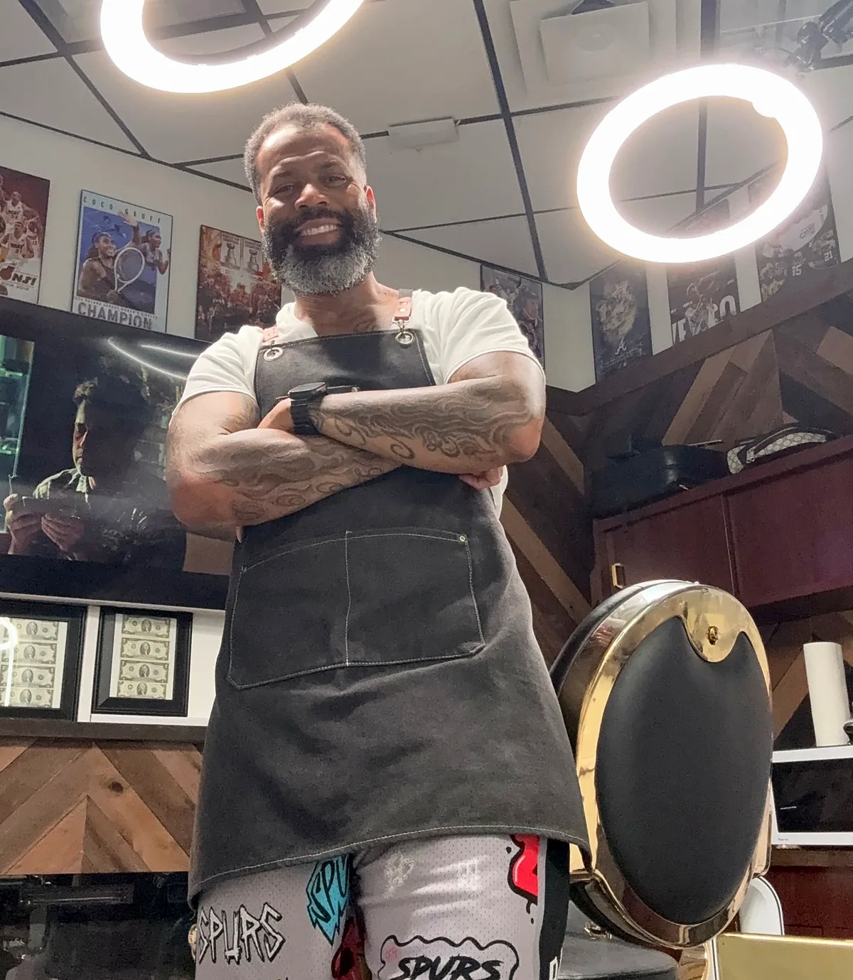 Anthony Hicks in his Palm Beach Gardens barbershop, arms crossed in his barber apron beside the gold barber chair